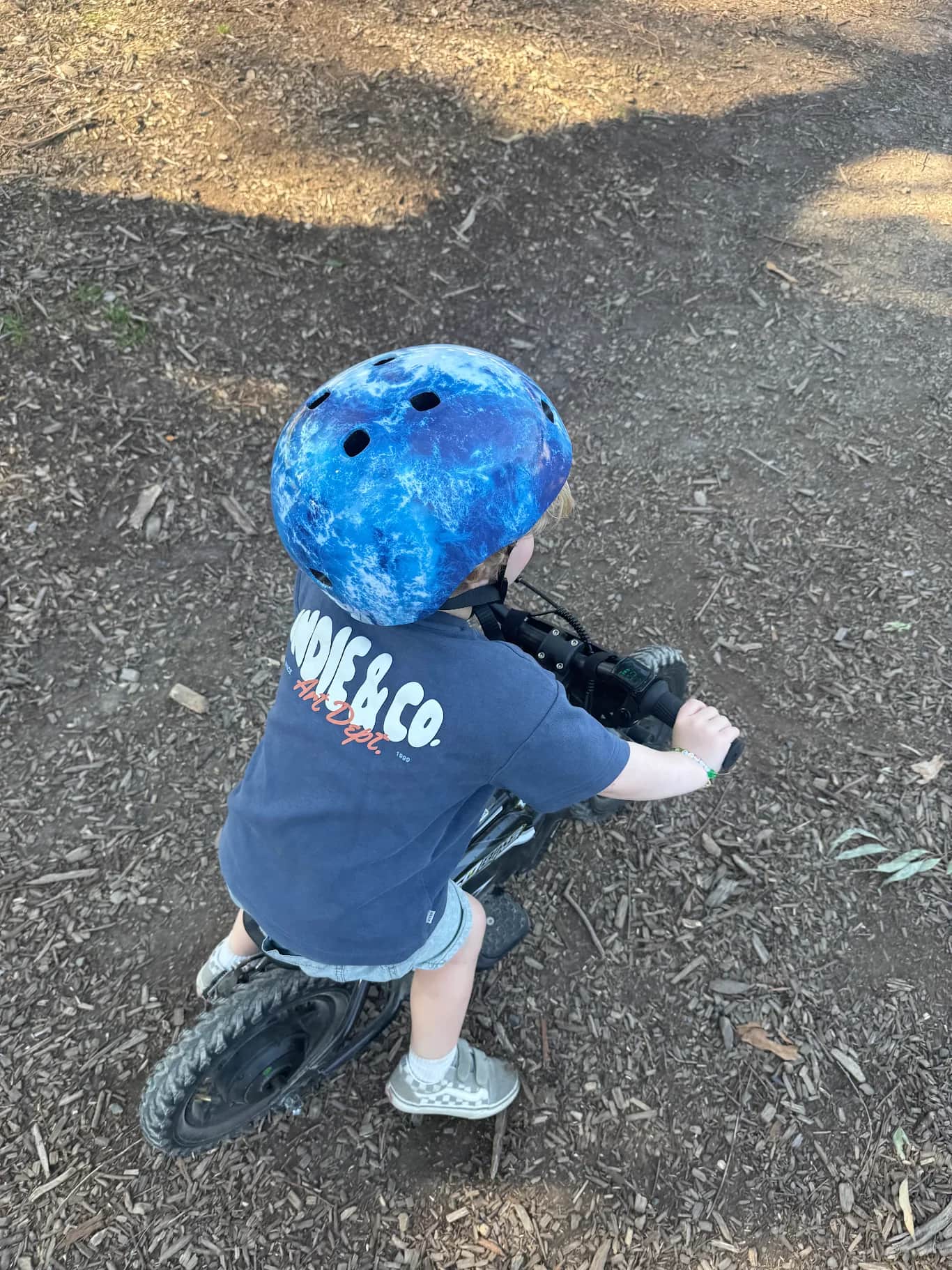 Young boy in a blue helmet riding his GoBike 12 along a bark-covered park path