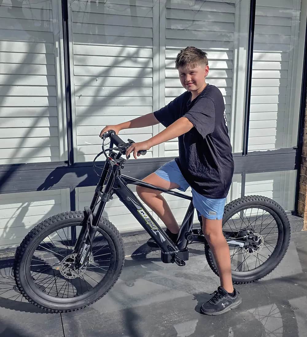 Teen rider sitting on his GoBike 24 electric bike outside a house