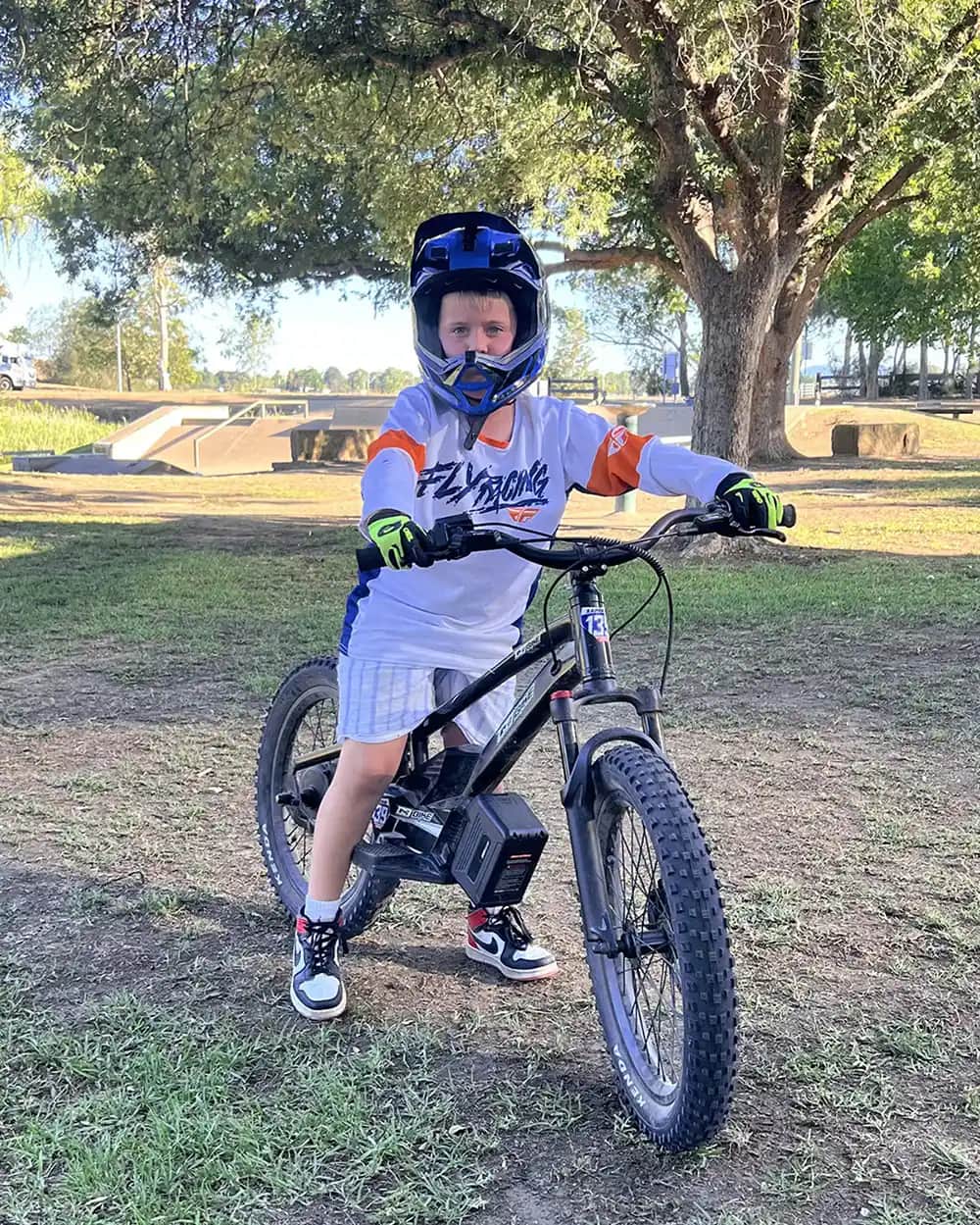 Boy in a full-face helmet standing over his GoBike 20 electric dirt bike for kids in a park