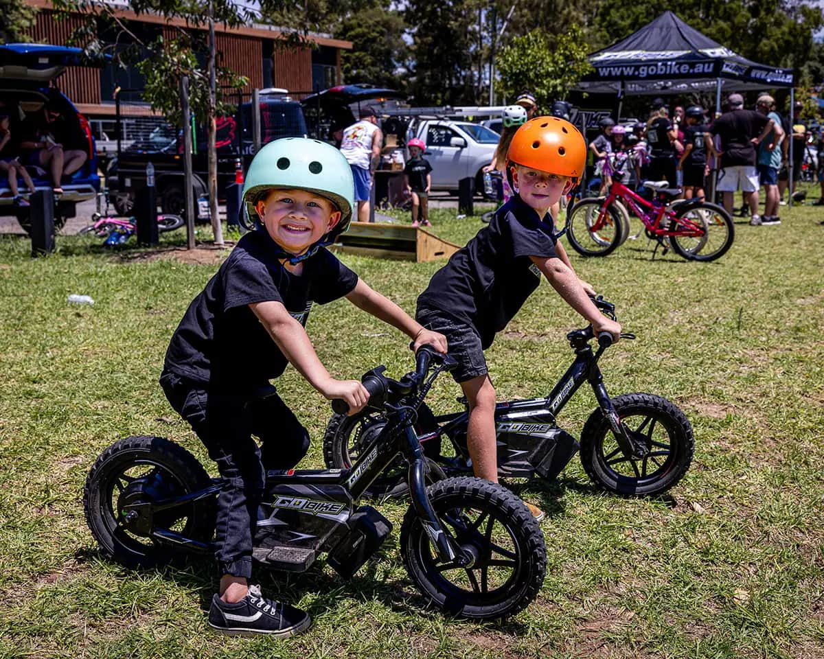 Two kids having fun on their GoBike 12 electric balance bikes at a park event