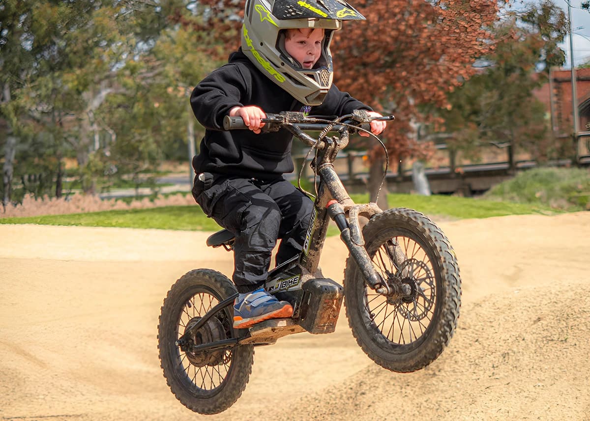 Kid catching air on a Gobike 16 electric dirt bike on an off-road trail.