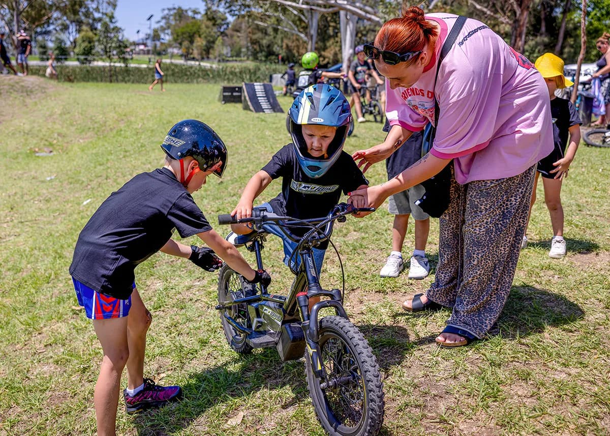 A child learning to ride the Gobike 16 with family support in a park.