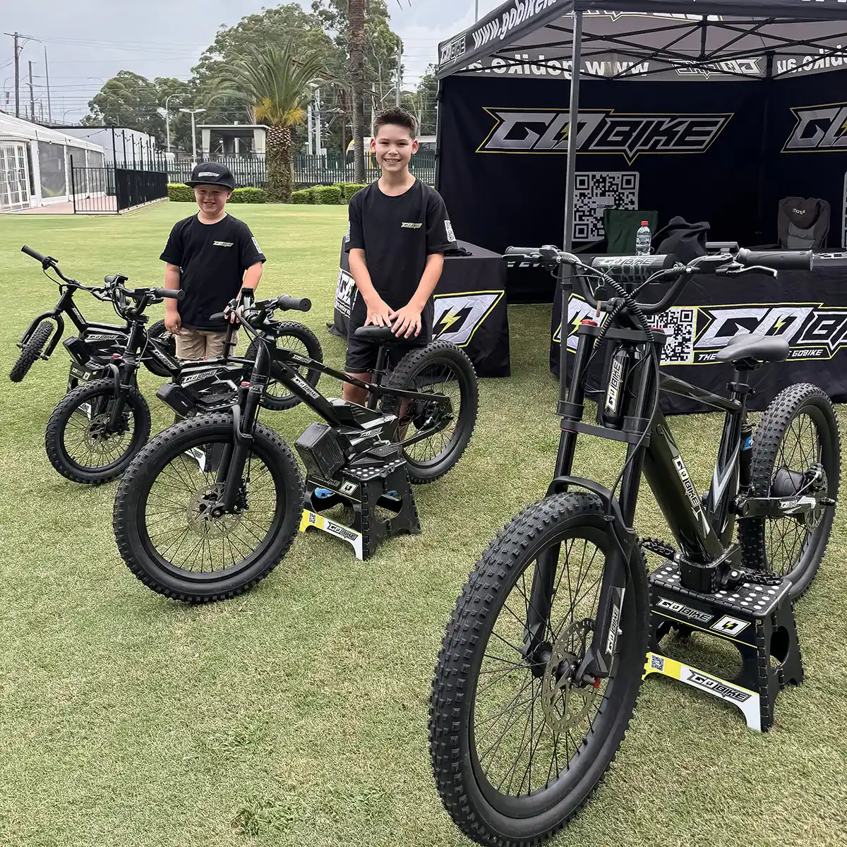 Three sizes of GoBike kids electric bikes lined up at the GoBike tent with smiling young riders
