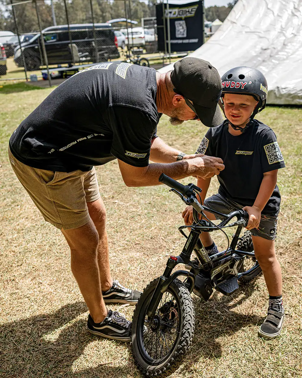 Adult checking a young rider's helmet strap before he rides his GoBike 16 kids e-bike