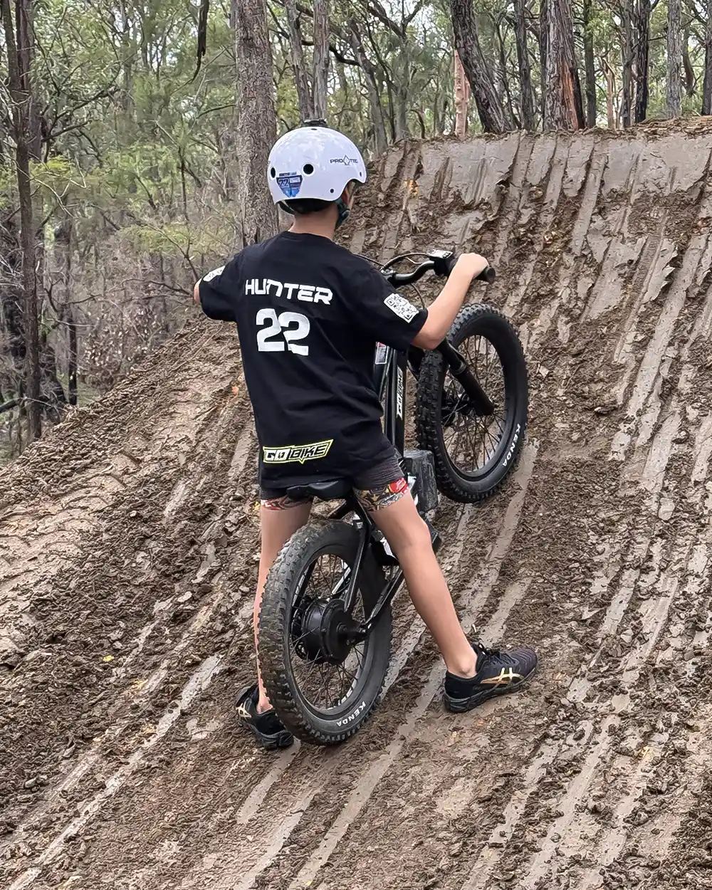 Kid pushing his GoBike kids electric bike up a steep, muddy dirt jump in the bush