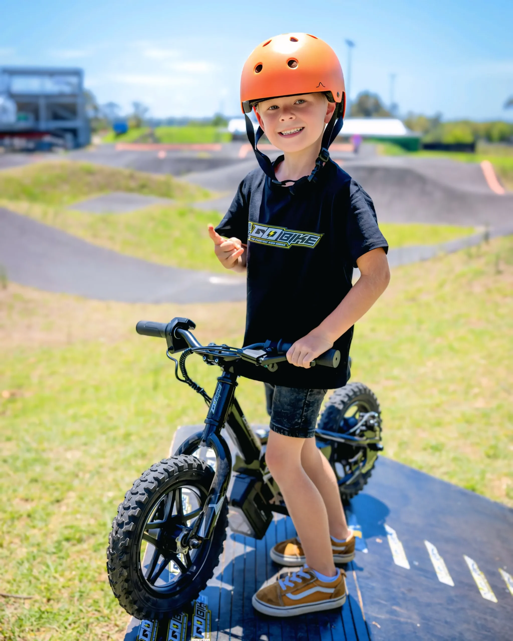 A smiling Australian child with a helmet enjoying a GoBike electric bike in a park