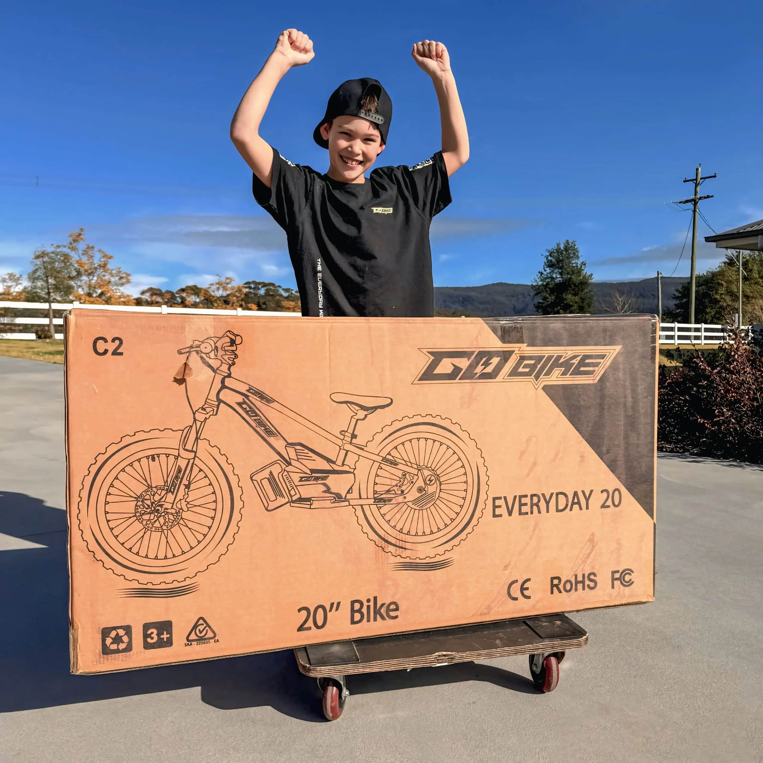 Excited boy celebrating behind the box his new GoBike 20 inch electric bike arrived in