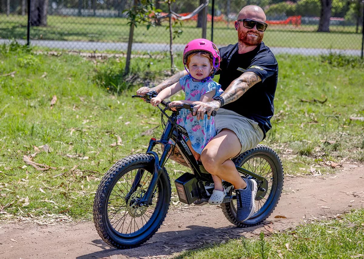 A father sharing a fun ride on the GoBike 20 with his young daughter in a park.
