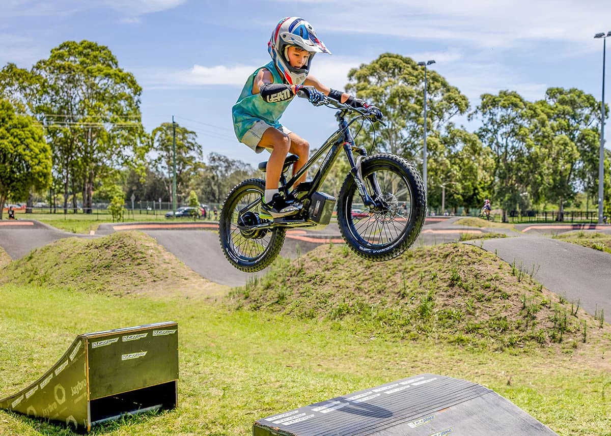 A young rider catching air on a jump with the GoBike 20 at a bike park.