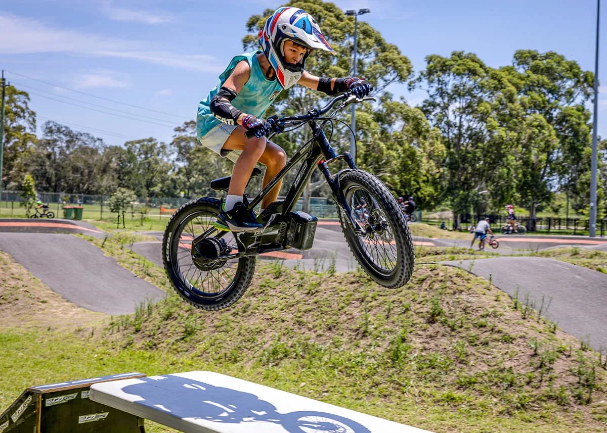 A young boy catching significant air while jumping his GoBike 20 off a wooden ramp.