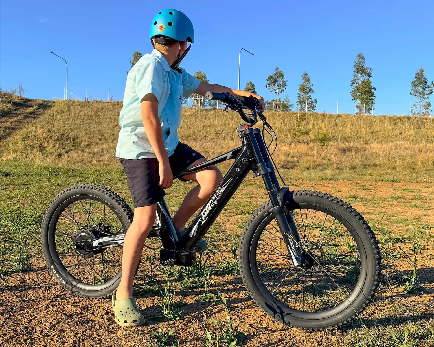 Teen in a blue helmet standing with his GoBike 24 in an open field