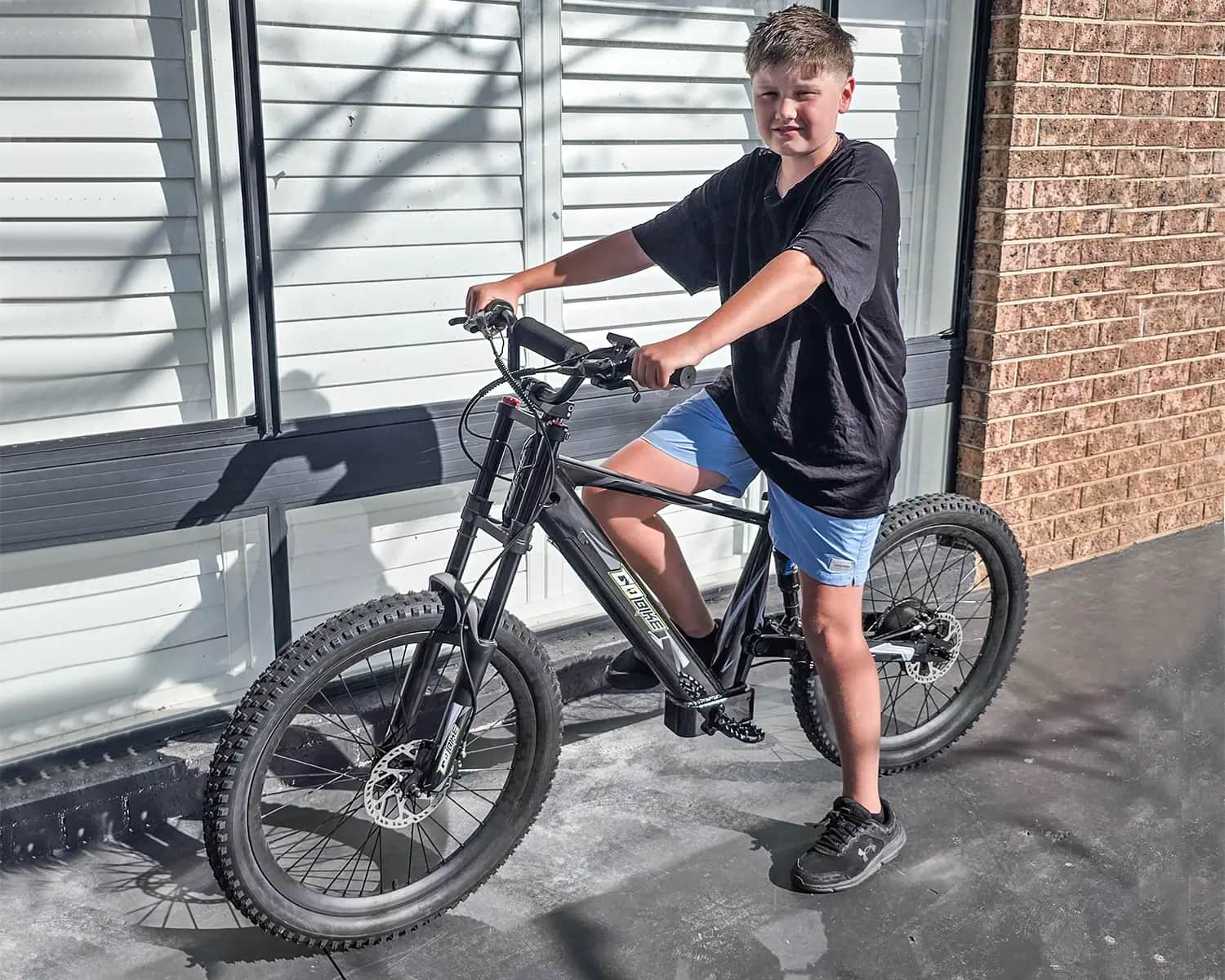 Teen standing with his GoBike 24 electric dirt bike outside his home