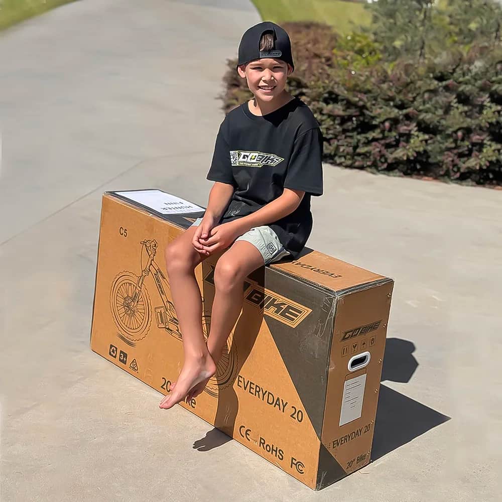 Boy sitting on a GoBike 20 delivery box. Every GoBike model, including the GoBike 24, ships in one box like this