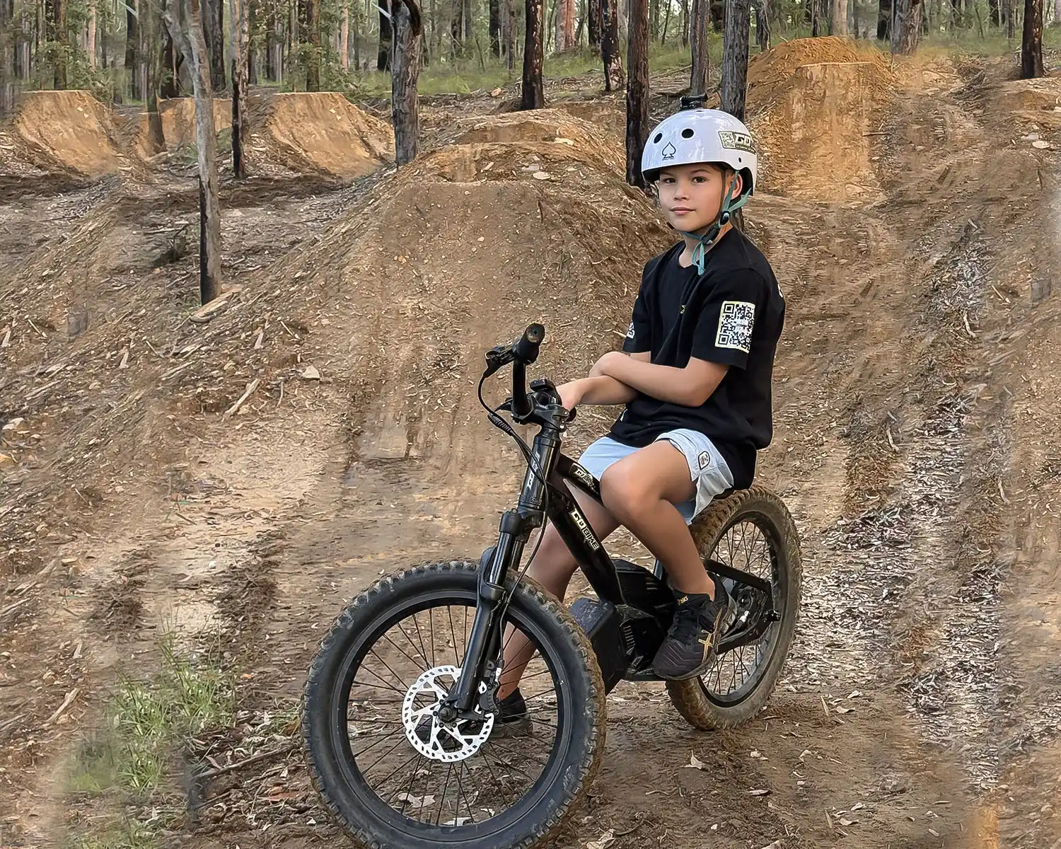 Boy sitting on his GoBike 20 kids electric dirt bike at a forest dirt jump trail