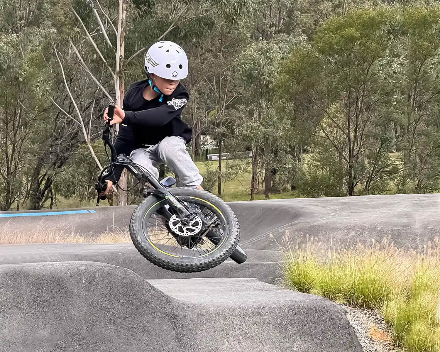 Rider lifting the front wheel of a GoBike 20 inch electric bike for kids over a pump track roller