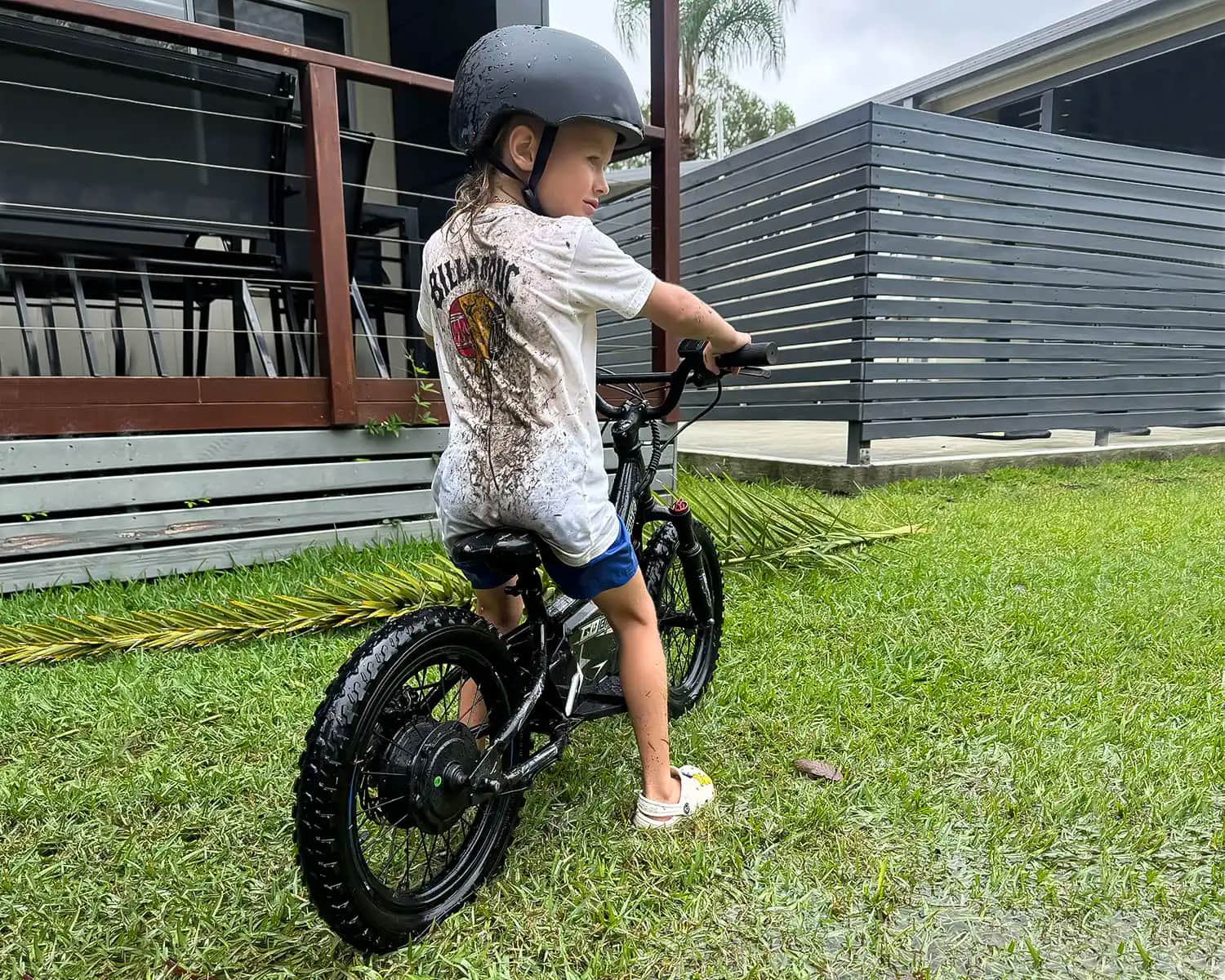 Young rider in a mud-splashed T-shirt sitting on a GoBike 16 in a wet backyard