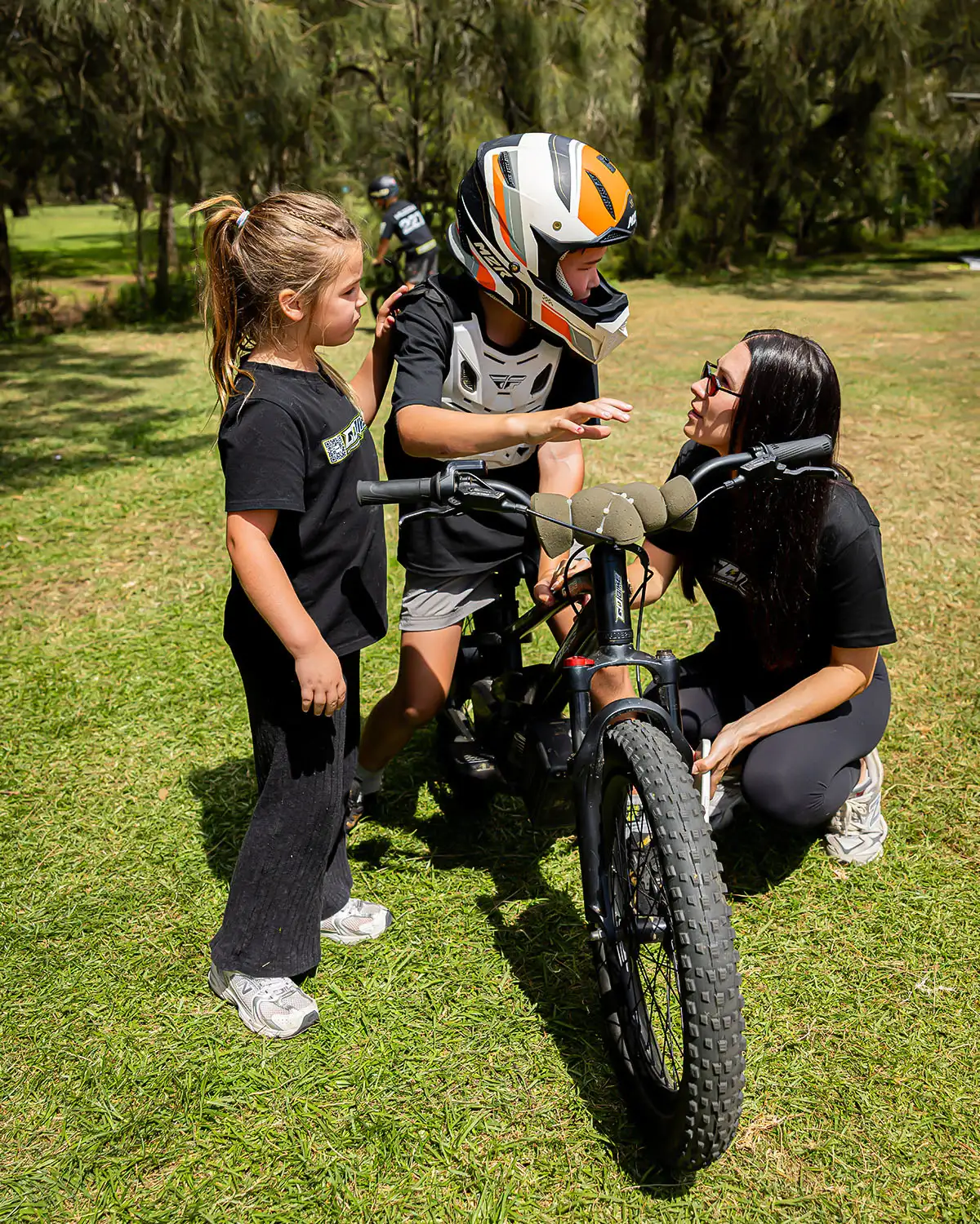 Mum encouraging her son in full safety gear on his GoBike 20 kids electric motorbike as his sister watches