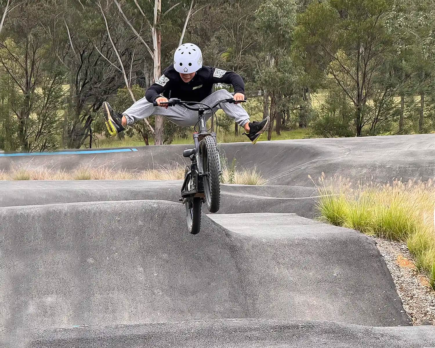 Kid doing a no-footer trick on a GoBike 20 electric dirt bike for kids at a pump track