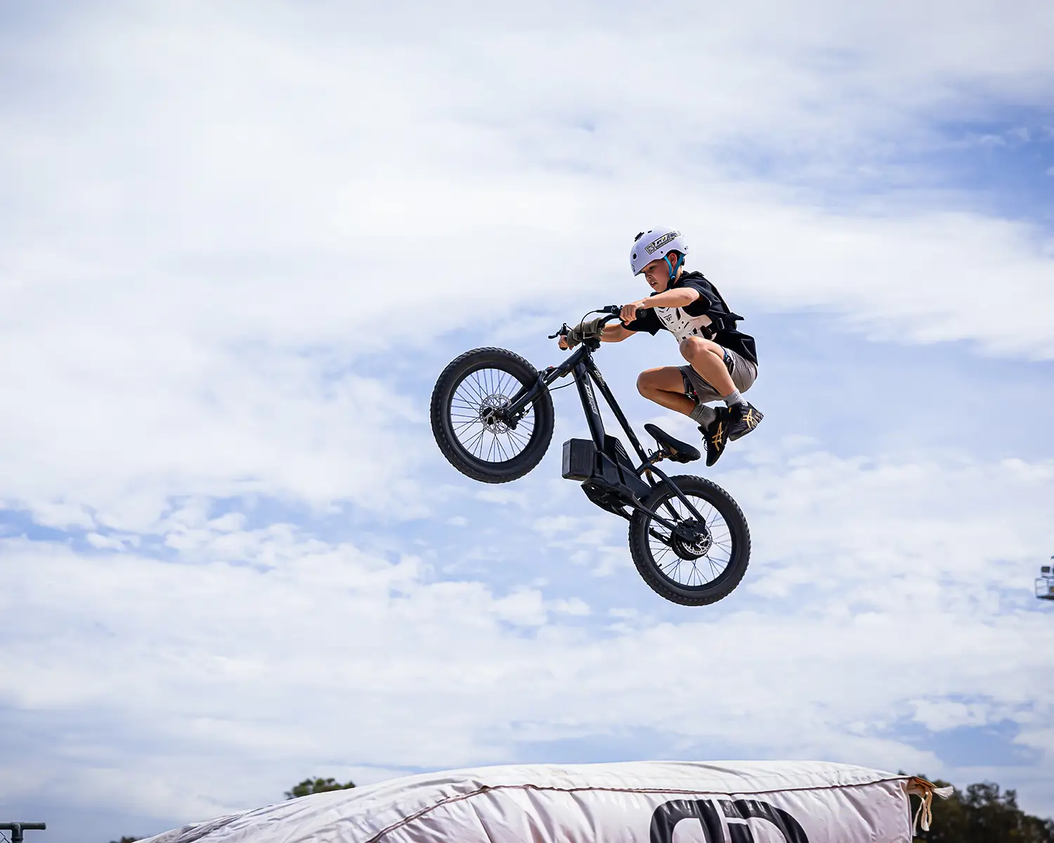 Kid in a white helmet doing a tuck jump over an airbag on a GoBike 20 kids electric dirt bike